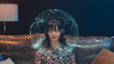 A woman with her eyes closed listening to music on headphones - dots of light around her head represent 360 Reality Audio