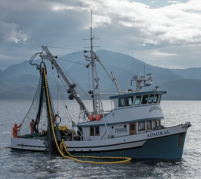 Hình ảnh một tàu đánh cá hồi - có tên là Admiral - với dãy núi Alaska phía sau vào một ngày trời yên tĩnh.