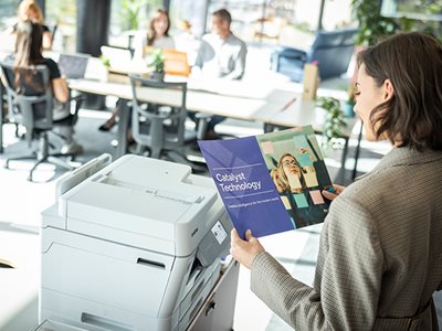 A woman reviewing print output while stood next to a Brother MFC-J6977DW in an office environment