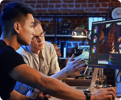Two men focus intently on color grading a video on a ProArt monitor in a warmly lit office with brick walls, conveying collaboration and concentration.