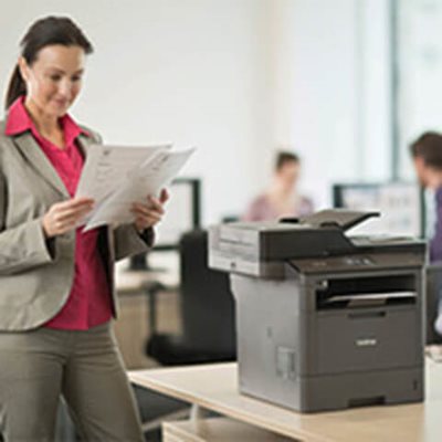 Woman standing by multifunction printer, reviewing printed double-sided multi-page document