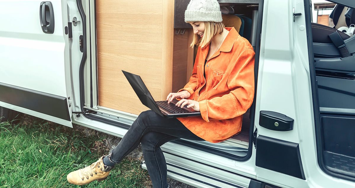 A woman working remotely on a laptop while sitting in a camper van, representing a van life setting.