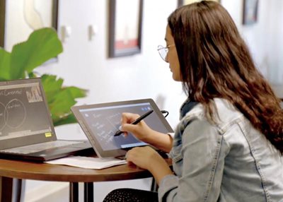 a woman using a stylus on a pen display connected to a laptop