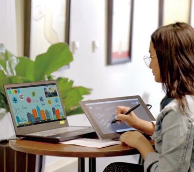a woman writing on the pen display connected to a laptop
