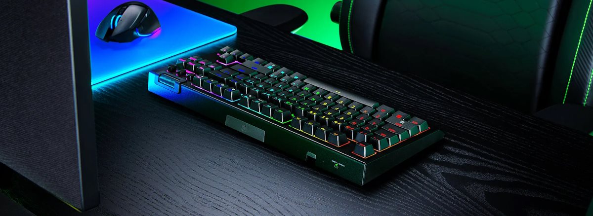 Gaming desk setup with RGB backlit mechanical keyboard, mouse on a glowing mouse pad, and gaming chair with green accents.