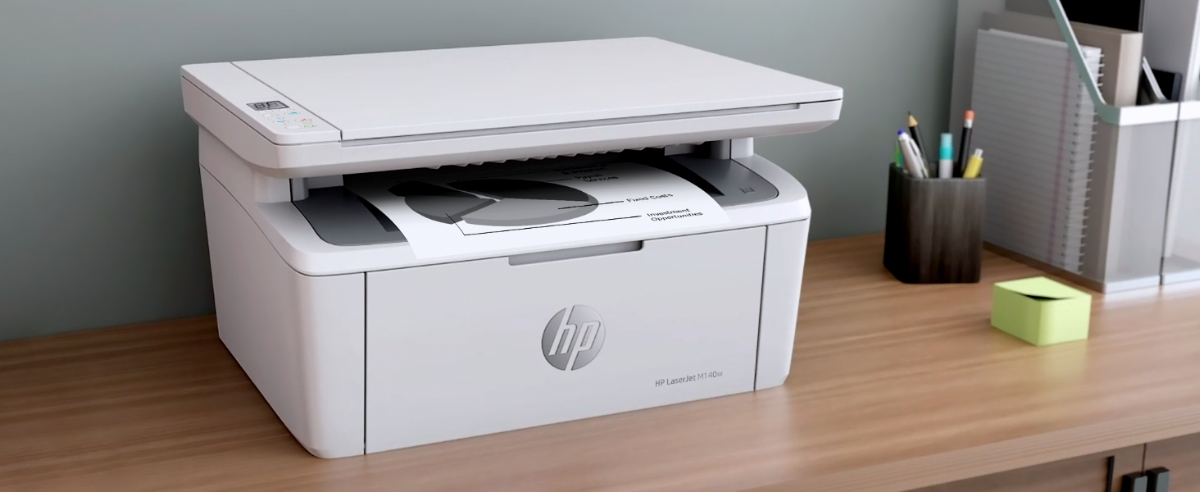 An HP LaserJet M140w printer outputting a document on a desk with office supplies.