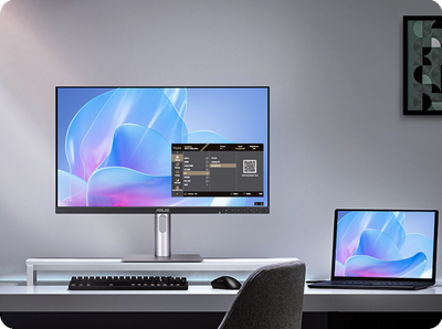 A modern desk setup with a ProArt monitor and a laptop displaying the same abstract blue and pink design. A keyboard and mouse are on the desk. The ambiance is sleek and minimalist.