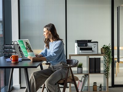 A woman holding colour print output while sat at a desk in an office environment