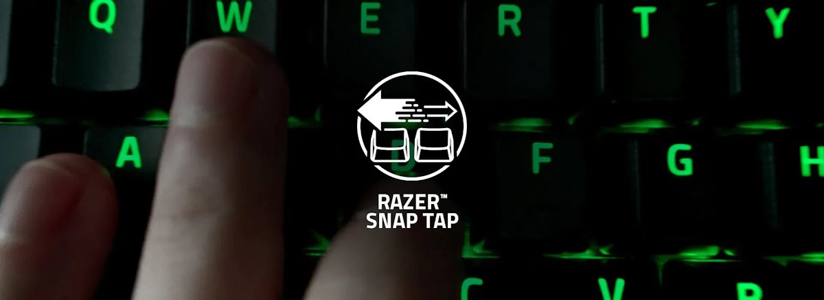 Finger presses the 'A' key on a backlit keyboard with green LEDs, displaying the Razer Snap Tap logo on the screen.