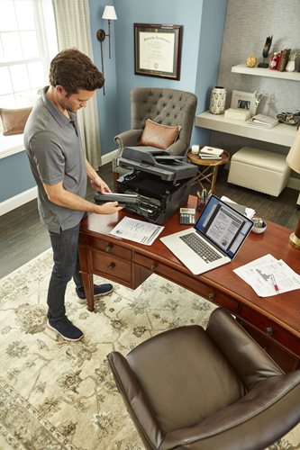 Man standing at desk in home office, loading new drum unit into a multifunction laser printer