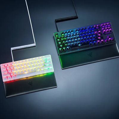 Two illuminated gaming keyboards with RGB backlit keys, one with a white frame and the other with a black frame, on a dark surface.