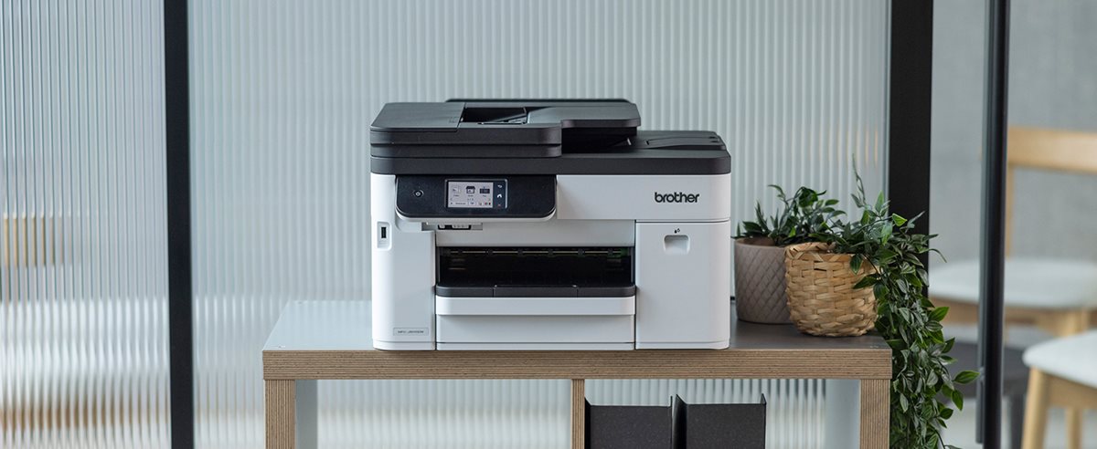 A Brother MFC-J5010DW on a shelving unit in front of a glass wall in an office environment