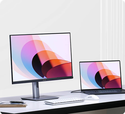 A desk setup with a ProArt monitor and a laptop, both displaying colorful abstract shapes.