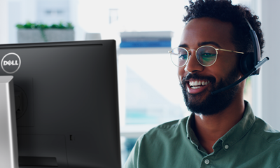 Bild eines lächelnden Mannes, der ein grünes Hemd und eine Brille mit einem Headset auf dem Kopf trägt und einen Dell Monitor verwendet.