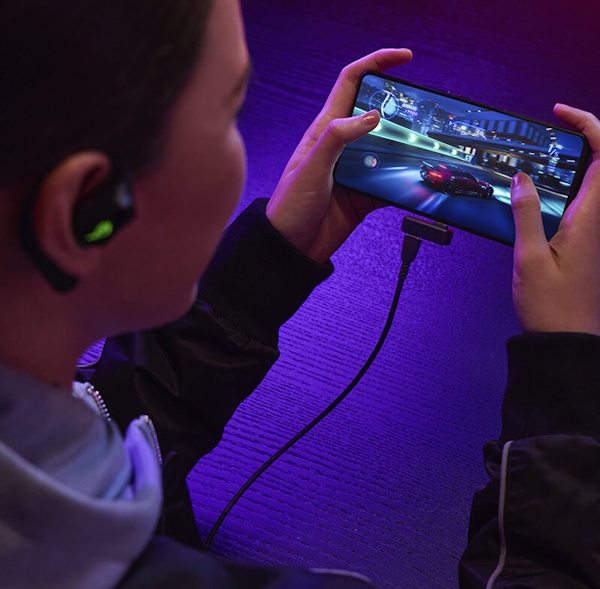 Eine Frau spielt auf ihrem Smartphone, während sie das ROG Cetra Open Wireless über USB-C Pass-Through Charging auflädt