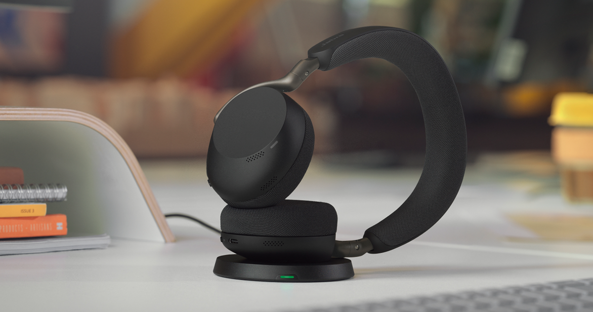 Sort Jabra Evolve3 75-headset, der hviler på sin ladestand på et skrivebord, med en blødt sløret kontorbaggrund.